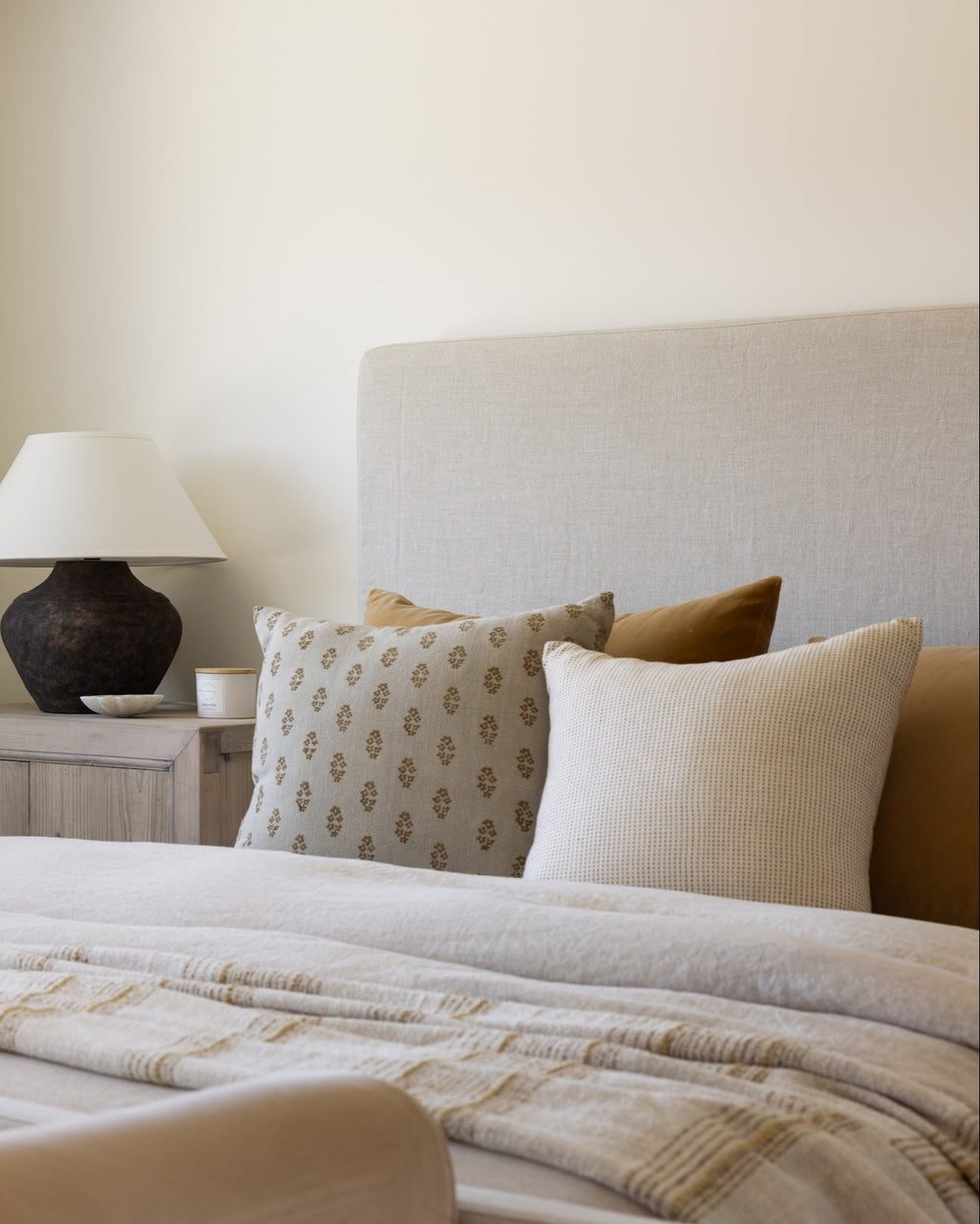 Bedroom with a bed featuring patterned and solid pillows, a lamp on a nightstand, and neutral walls.
