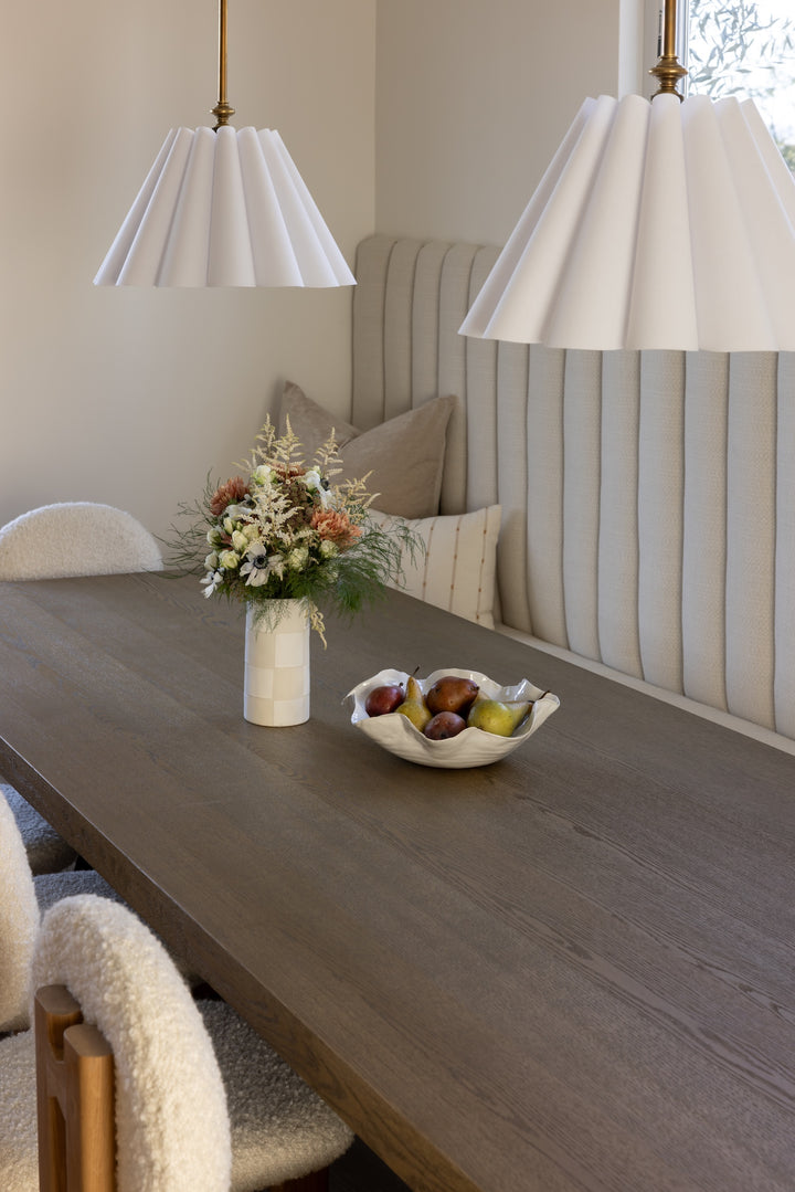 Dining room with a table set with a vase of flowers and a fruit bowl, surrounded by chairs and a striped wall.